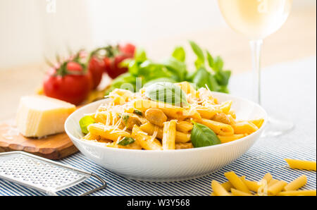 Pasta penne con pezzi di pollo funghi basilico formaggio Parmigiano e vino bianco. La cucina italiana in piastra bianca sul tavolo da cucina. Foto Stock