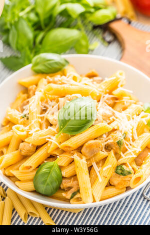 Pasta penne con pezzi di pollo funghi basilico formaggio Parmigiano e vino bianco. La cucina italiana in piastra bianca sul tavolo da cucina Foto Stock