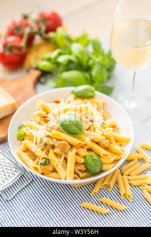 Pasta penne con pezzi di pollo funghi basilico formaggio Parmigiano e vino bianco. La cucina italiana in piastra bianca sul tavolo da cucina. Foto Stock