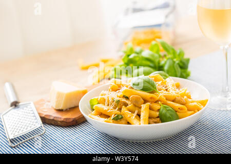 Pasta penne con pezzi di pollo funghi basilico formaggio Parmigiano e vino bianco. La cucina italiana in piastra bianca sul tavolo da cucina. Foto Stock