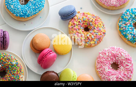 Ciambelle e macarons francese sul tavolo bianco, vista ravvicinata con i dettagli, vista dall'alto Foto Stock