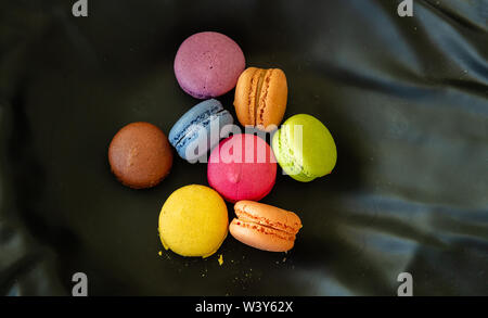 Macarons colori pastello con crema di cioccolato su sfondo nero, vista ravvicinata con i dettagli, vista dall'alto Foto Stock