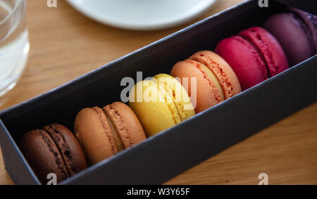 Macarons colori pastello in una carta nera scatola regalo, sfondo legno, vista ravvicinata con i dettagli Foto Stock