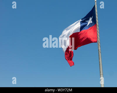 Bandiera del Cile vola in un vento forte contro un luminoso cielo blu con i riflessi del sole. Simbolo patriottico del Cile, America del Sud. Foto Stock