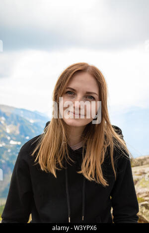 Le donne in cima alla montagna. Giovane ragazza bionda viaggiatore con un zaino blu sollevato e godendo il verde paesaggio di montagna. Vista posteriore Foto Stock