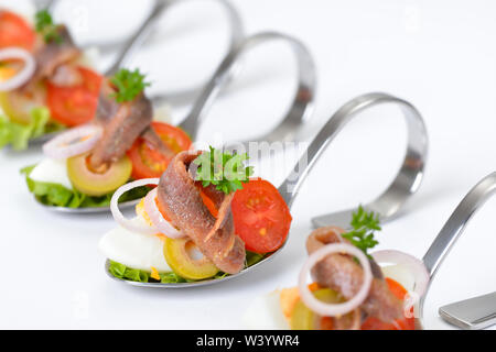 Raffinati antipasti di pesce con i filetti di acciuga e uova a servire i cucchiai collocati su uno sfondo bianco Foto Stock