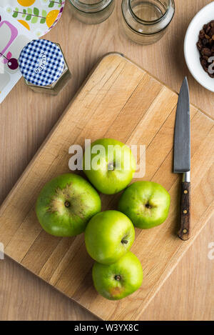 Bramley mele sulla tavola di legno con coltello, vasetti di etichette e altri ingredienti per rendere chutney. Foto Stock