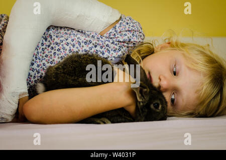 Hurt ragazza bionda con mano rotto giacente in cattivo e azienda bunny rabbit pet Foto Stock