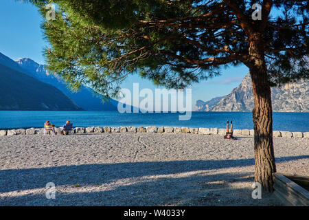 Turisti che si siedono sulla spiaggia a piccolo porto Porticcioloat Lago di Garda, il Lago di Garda in Torbole - Nago, Riva, Trentino , Italia al 15 aprile 2019. © P Foto Stock