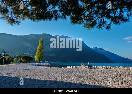 Turisti che si siedono sulla spiaggia a piccolo porto Porticcioloat Lago di Garda, il Lago di Garda in Torbole - Nago, Riva, Trentino , Italia al 15 aprile 2019. © P Foto Stock