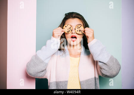 A seguito di una ricetta di cucina. Bella ragazza che coprono gli occhi con i cookie. Ragazza carina per divertirti con i cookie. Stile panificio Chocolate Chip Cookie ricetta. Cuocere in forno Foto Stock