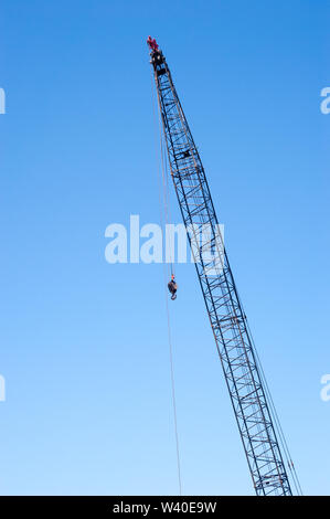 Tall industrial gru sul cielo blu chiaro, con cavi e gancio da appendere le pulegge superiore. Foto Stock