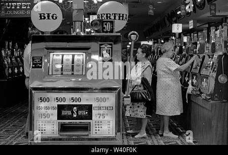 Una macchina da frutta banditi armati slot machine, donne che giocano a gioco d'azzardo. Big Bertha un gigantesco bandito a un braccio in una Penny Arcade. 1969, Reno Nevada Casino. USA 1960 STATI UNITI OMERO SYKES Foto Stock
