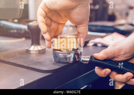 Vista dettagliata del barista mani con distributore di caffè per premere il caffè macinato in portafilter per fare caffè espresso bevanda calda. Piccole imprese locali lavorano in CAF Foto Stock