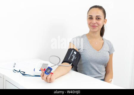 Giovani sorridente ragazza bella misure del polso e della pressione sanguigna presso la reception di un terapeuta. Foto Stock