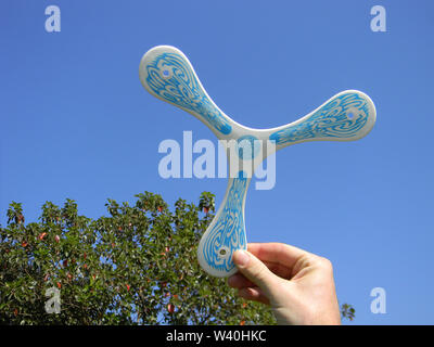 Mano d'uomo in plastica con il boomerang di leggere al volo su un cielo blu. Foto Stock