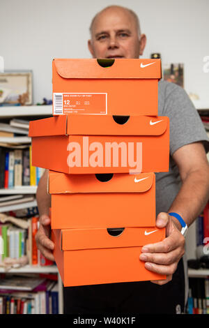 Parigi, Francia - Luglio 10, 2019: atleta senior man tenendo in mani più cartoni rosso con le scarpe da running Nike nel soggiorno dopo l'e-commerce online order Foto Stock