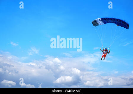 Paracadutista con una tettoia blue di un paracadute sullo sfondo di un cielo blu e nuvole, close-up. Paracadutista paracadute sotto al di sopra delle nuvole temporalesche Foto Stock