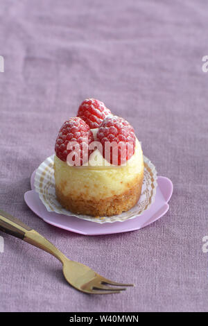 Deliziosi mini Cheesecake ai lamponi e rosa sul cupcake stand su viola pallido sfondo di lino. Il fuoco selettivo sulla parte anteriore di lamponi. Formato verticale con Foto Stock