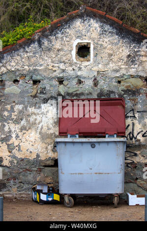 Un cassonetto accanto a una casa vecchia facciata con una piccola finestra che guarda come rovine Foto Stock