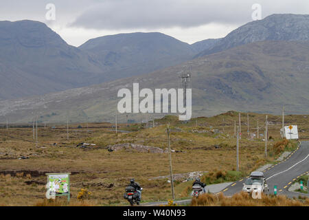 Viaggiando su strada in Irlanda rurale con le motociclette e veicoli su strada asfaltata nella Contea di Galway con montagne in Connemara si vede attraverso bog terra. Foto Stock