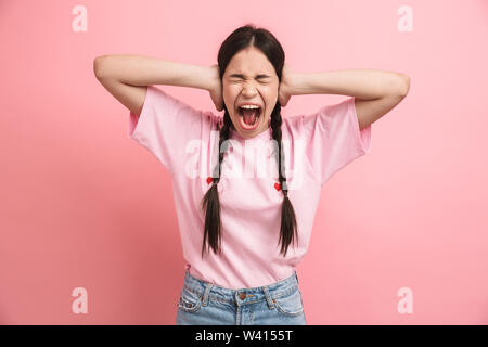 Immagine di scioccato teen ragazza con due trecce urlando a telecamera e che copre le sue orecchie con le mani isolate su sfondo rosa Foto Stock