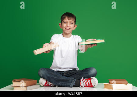 Felice ragazzo con lentiggini dando libri presso la fotocamera su sfondo verde Foto Stock