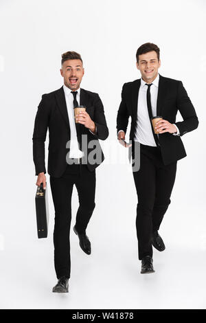 Due attraenti sorridente fiducioso imprenditori indossando tute in esecuzione isolate su uno sfondo grigio, tenendo il caffè da asporto Foto Stock