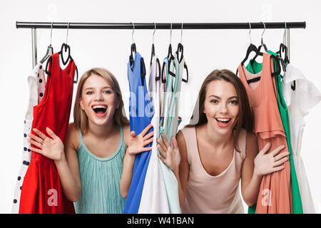 Due allegro ragazze giovani isolate su sfondo bianco, scegliendo abiti su un portabiti Foto Stock