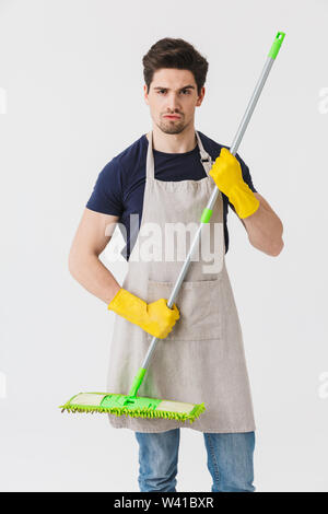 Foto del maschile giovane uomo giallo da indossare guanti di gomma per protezione mani tenendo mop durante la pulizia casa isolata su sfondo bianco Foto Stock
