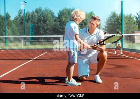 Curly boy ascolto di papà prima di giocare a tennis Foto Stock