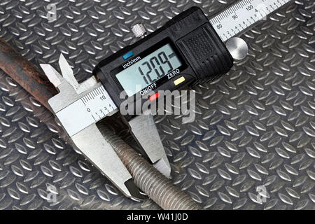 La misurazione di una filettata dello stelo in acciaio con calibro digitale su metallo ondulato sullo sfondo Foto Stock