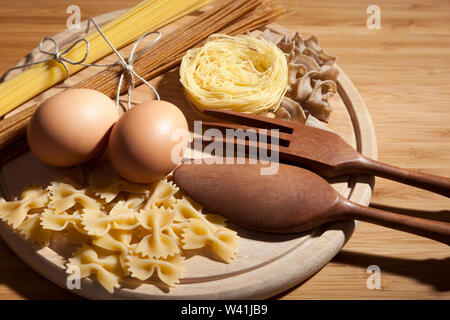 Composizione con diversi tipi di pasta, uova e cucina in legno impostare posta sul round tagliere Foto Stock