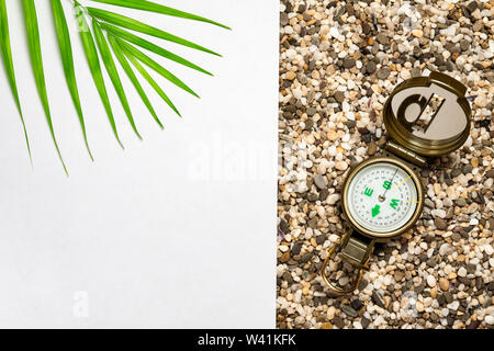 Tema turistico, spiaggia sabbiosa, bussola, ramo di una felce, sfondo bianco per l'iscrizione. Foto Stock