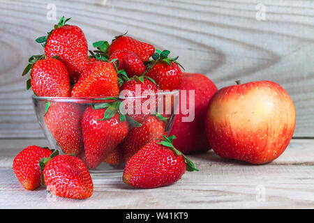 Fragole in piatti, sullo sfondo sono mele. Tutto su uno sfondo di legno da vicino Foto Stock