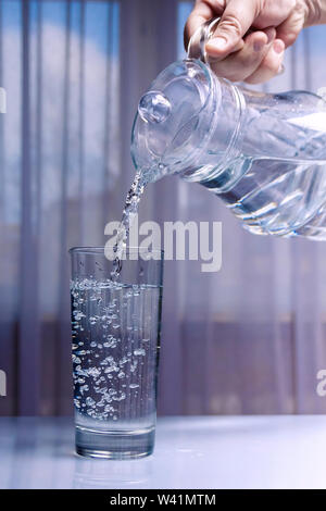 L'acqua viene versata in un bicchiere da un decanter di vetro. Sfondo chiaro non uniforme Foto Stock