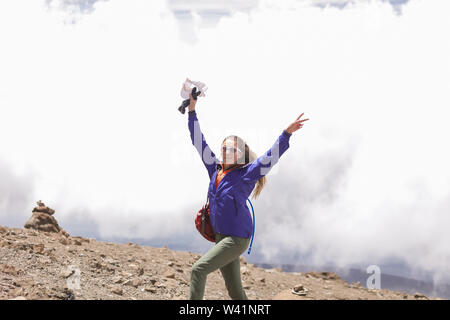 Energica ragazza attivo che posano per una foto sul bianco delle nuvole sullo sfondo. In piedi sulla cima del Kilimanjaro con le mani alzate. Tenendo un cappuccio bianco Foto Stock