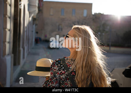 Giovane donna bionda che camminando per le strade a La Valletta, Malta, vista posteriore Foto Stock