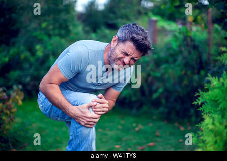 Persone, sanitario e problema concetto - close up di un uomo infelice che soffrono di dolore nella gamba o al ginocchio per esterno Foto Stock
