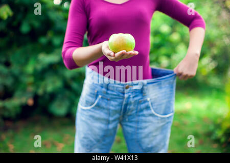 Giovane donna indossa grandi jeans allentati con Apple in mano outdoor- perdita di peso concept Foto Stock