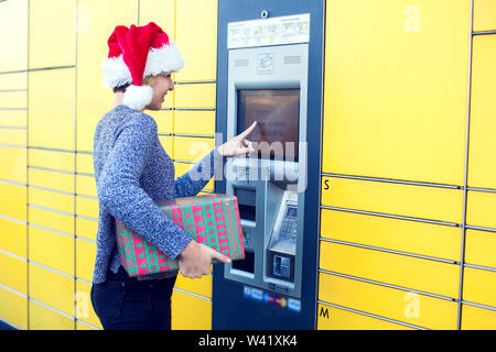 Donna con santa natale hat client utilizzando automated self service post macchina terminale o armadietti per il deposito del pacco per lo storage Foto Stock