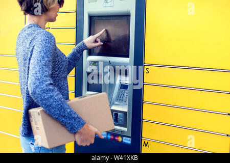 Donna client utilizzando automated self service post macchina terminale o armadietti per il deposito del pacco per lo storage Foto Stock