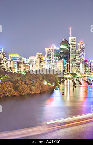 Paesaggio urbano di notte e il cielo blu scuro con una foresta di illuminazione luci luminose dietro un fiume e riflessi colorati a Brisbane, Queensland, Australia. Foto Stock