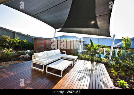 Area patio esterna con banchi di bianco e pavimento in legno in una giornata di sole, che ha anche ricoperto con una capanna dal tetto sopra le spalle e pannelli di vetro Foto Stock