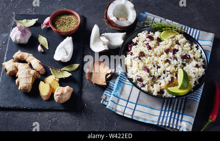 Il giamaicano di riso e fagioli rossi cotti con latte di cocco aromatizzato con aglio, cipolle e spezie creole in una ciotola con gli ingredienti su di un nero ardesia vassoio, h Foto Stock