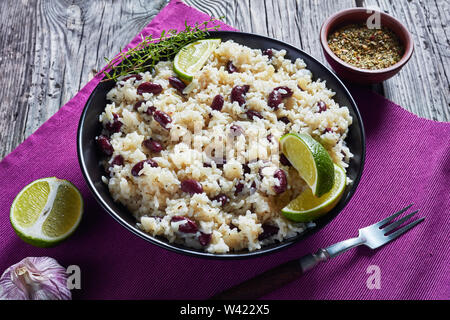 Caraibi riso e fagioli rossi cotti con latte di cocco aromatizzato con aglio, cipolle e spezie creole in una ciotola su una tabella mat su un vecchio tavolo di legno, v Foto Stock