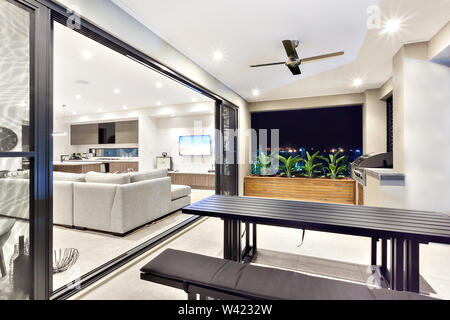 Al di fuori dell area patio con tavoli e panche accanto a gas cabinet grill accanto a piante attaccata al soggiorno moderno Foto Stock