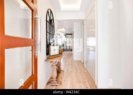 Porta di legno entrata di una casa moderna attraverso il corridoio, tra cui la tradizionale guarda e vaso di fiori sul tavolo con piano in legno Foto Stock