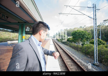 Imprenditore in attesa del treno e guardando a guardare, luce solare intorno alla zona, mattina il tempo e le ore di punta, il pavimento è piastrellato, sky è chiara. Foto Stock