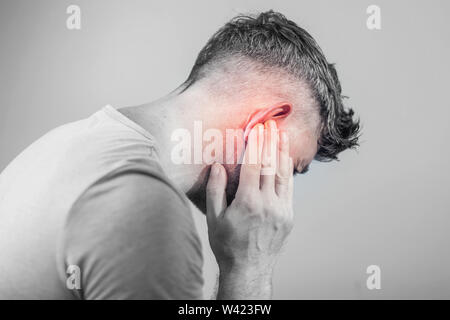 Di sesso maschile di dolore alle orecchie di toccare la sua dolorosa testa isolata su sfondo grigio Foto Stock